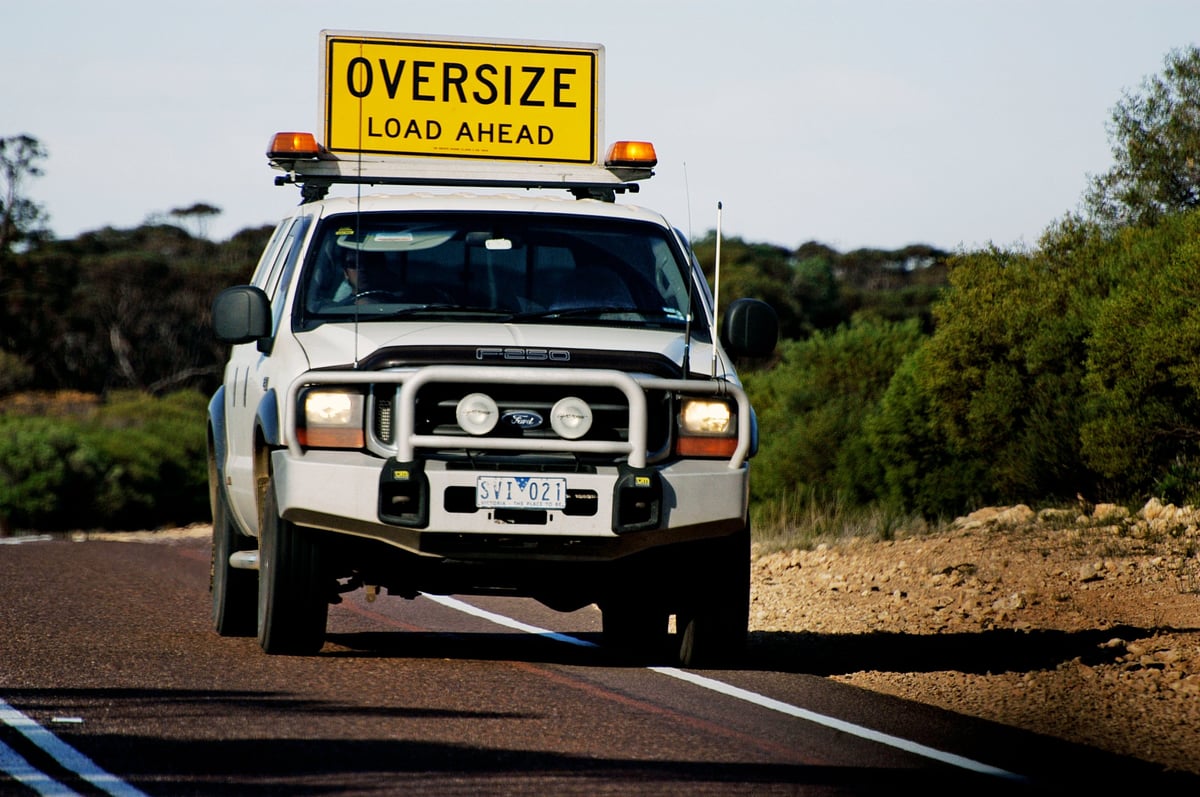 Safety car escorting a huge wide truck on a road